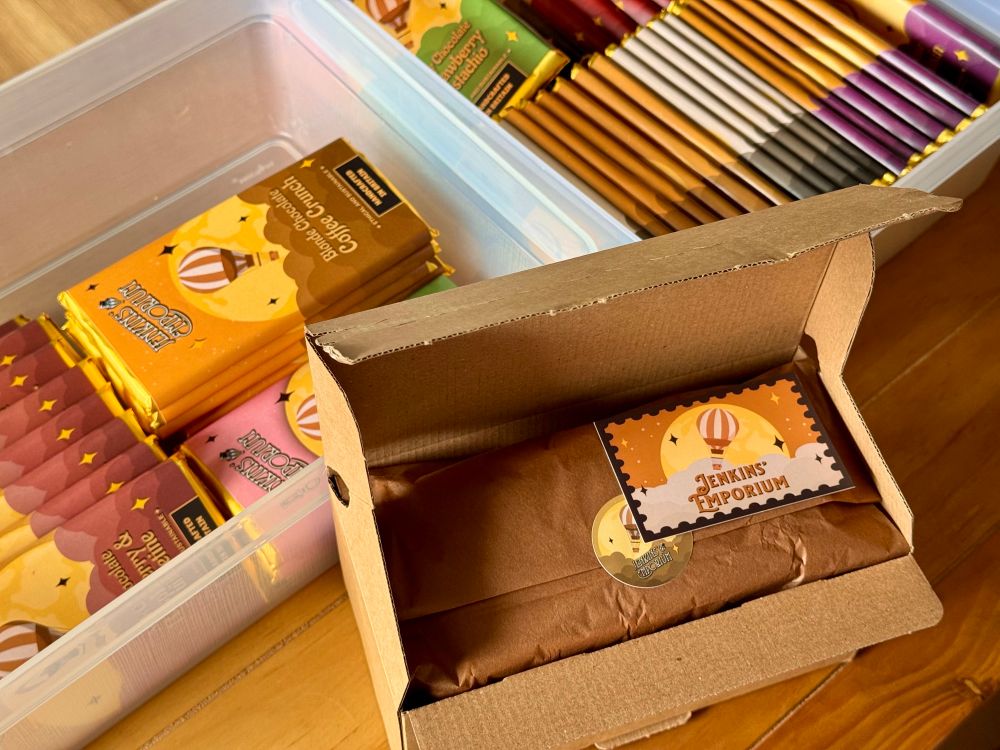A small parcel in which brown silk paper can be seen. A sticker and card with a hot hair ballon on them sit atop. Many chocolates bars in the background.