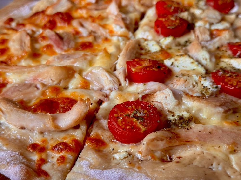 Close up of a pizza with a cream base, chicken, tomatoes, and cheese 