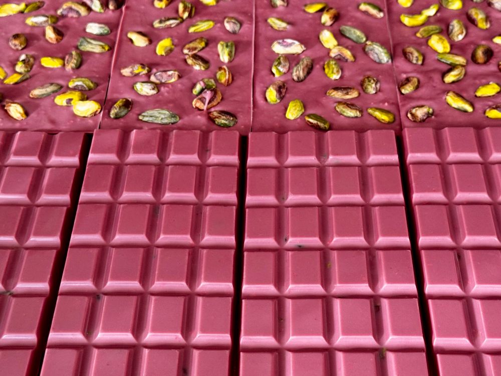 Front and back of many pink chocolate bars. The back is studded with pistachios.