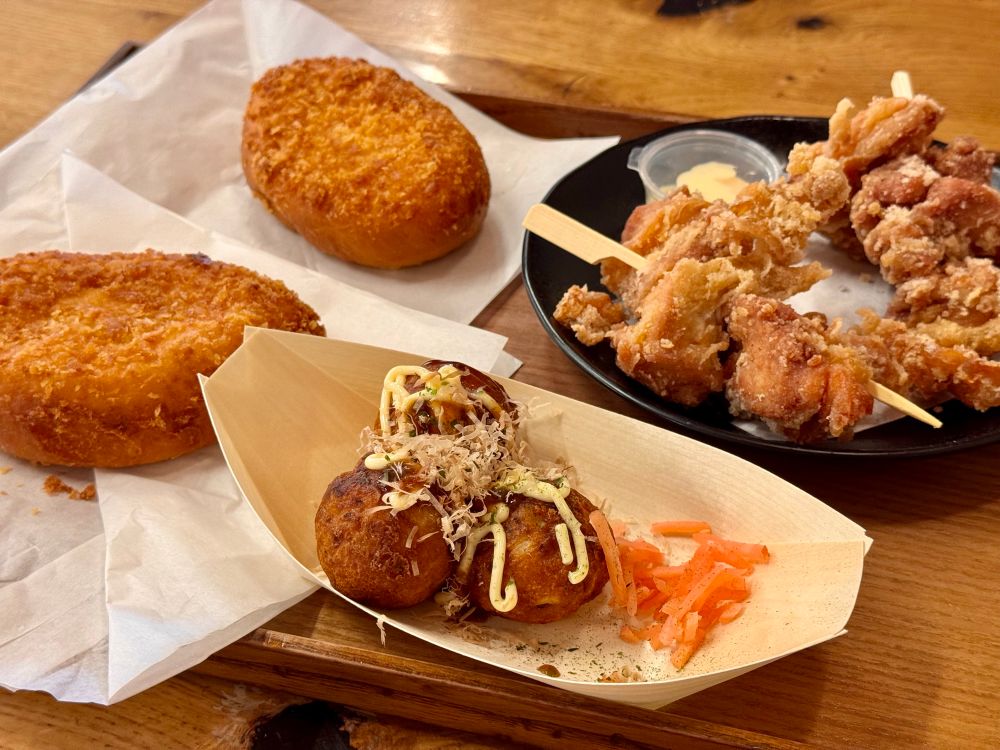 A tray with takoyaki, chicken skewers, and two curry breads