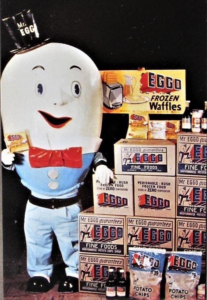 Vintage photo of the disturbing Mr. Eggo frozen waffles mascot standing beside a stack of Eggo products, daring you to run.