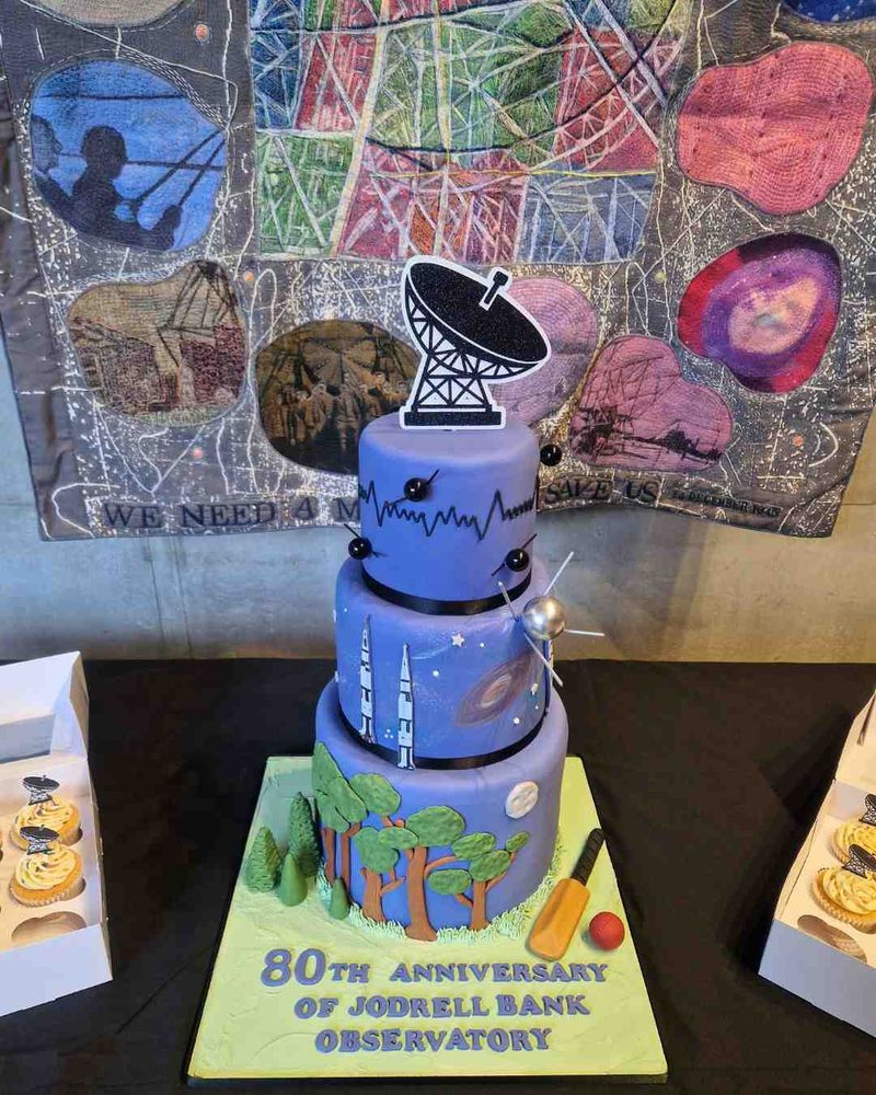 A cake celebrating the 80th anniversary of Jodrell Bank displayed in front of a preview of the 80th anniversary quilt, created by Anne Kelly.