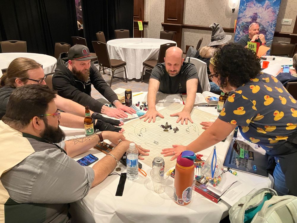 Raquel along with her four players all have hands placed in the center of the table as they join arcane forces to restore a prison to its healthy state