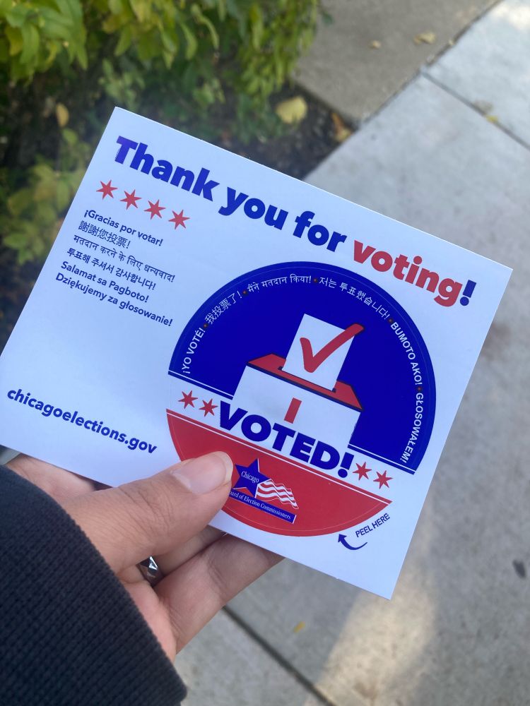 My hand holding up an election sticker as proof of participating in this year’s election.