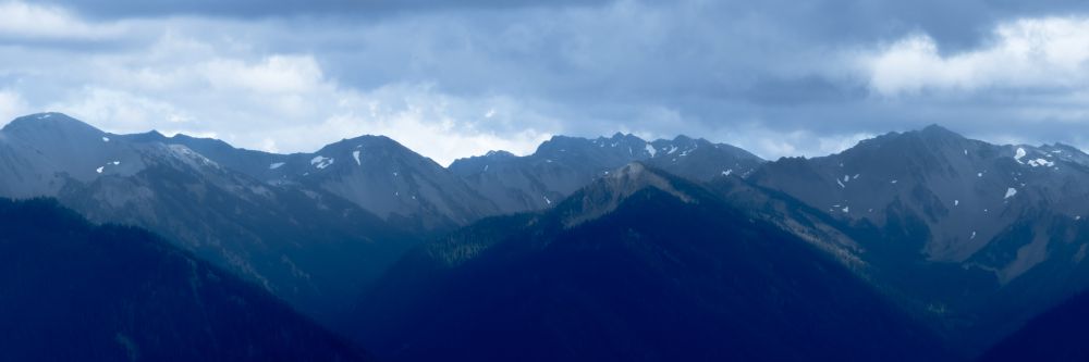 A mountain range tinted in blue light, overcast by clouds, with a bit of haze. 