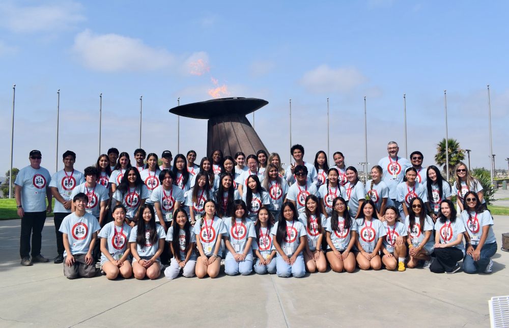 Red Cross youth and staff in matching t-shirts posing in front of an Olympic statue with a flame