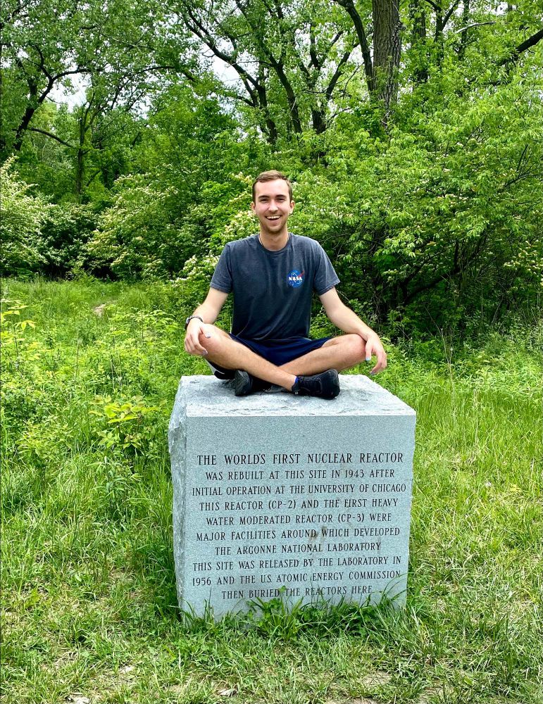 Me sitting with my legs crossed on a stone cube that reads: “THE WORLD'S FIRST NUCLEAR REACTOR WAS REBUILT AT THIS SITE IN 1943 AFTER INITIAL OPERATION AT THE UNIVERSITY OF CHICAGO THIS REACTOR (CP-2) AND THE FIRST HEAVY WATER MODERATED REACTOR (CP-3) WERE MAJOR FACILITIES AROUND WHICH DEVELOPED
THE ARGONNE NATIONAL LABORATORY
THIS SITE WAS RELEASED BY THE LABORATORY IN
1956 AND THE US ATOMIC ENERGY COMMISSION
THEN BURIED THE REACTORS HERE”