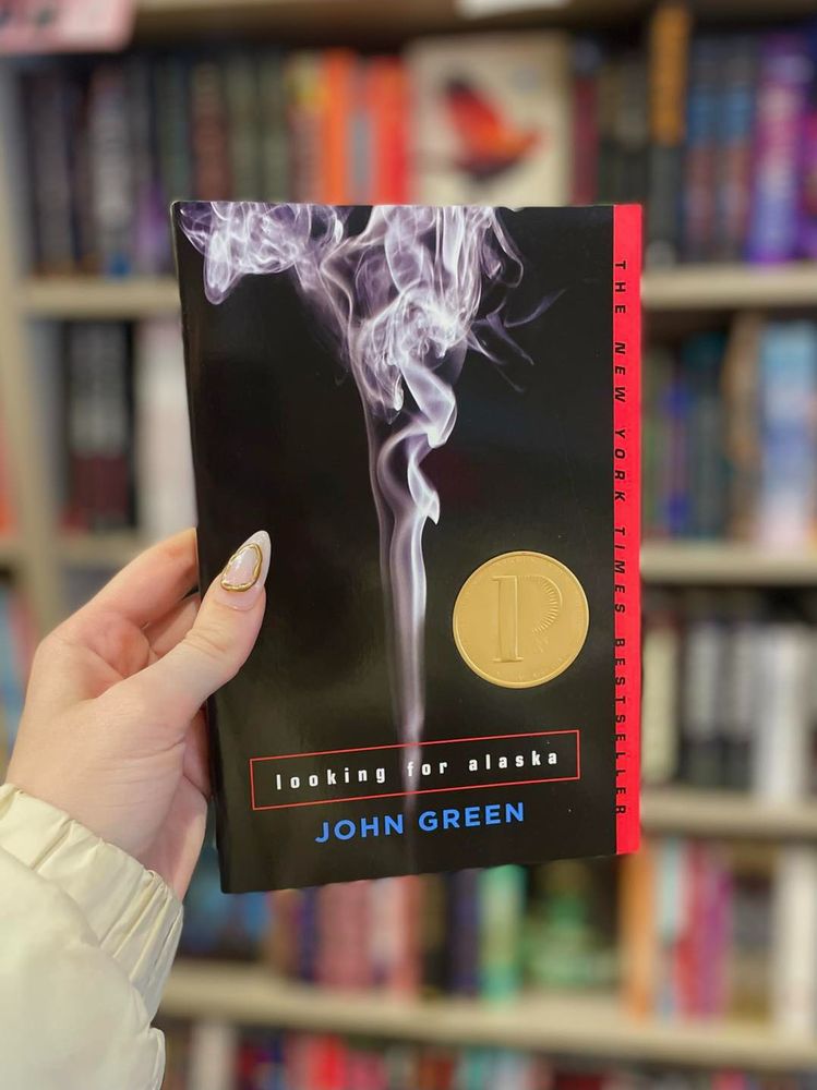 An image of a hand holding the book, "Looking for Alaska" by John Green.

https://www.blue-house-books.com/item/YbuqOsBAiIp4ROxpFKvEKg

The award-winning, genre-defining debut from John Green, the #1 bestselling author of The Anthropocene Reviewed and The Fault in Our Stars Winner of the Michael L. Printz Award • A Los Angeles Times Book Prize Finalist • A New York Times Bestseller • A USA Today Bestseller • NPR’s Top Ten Best-Ever Teen Novels • TIME magazine’s 100 Best Young Adult Novels of All Time • A PBS Great American Read Selection • Millions of copies sold!
 
First drink. First prank. First friend. First love.

Last words.
 
Miles Halter is fascinated by famous last words—and tired of his safe life at home. He leaves for boarding school to seek what the dying poet François Rabelais called the “Great Perhaps.” Much awaits Miles at Culver Creek, including Alaska Young, who will pull Miles into her labyrinth and catapult him into the Great Perhaps.

"Looking for Alaska" brilliantly chronicles the indelible impact one life can have on another. A modern classic, this stunning debut marked #1 bestselling author John Green’s arrival as a groundbreaking new voice in contemporary fiction.

Newly updated edition includes a brand-new Readers' Guide featuring a Q&A with author John Green