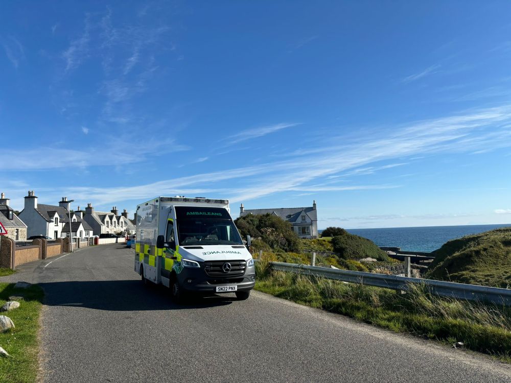 A parked ambulance next to the shoreline on a very sunny day.