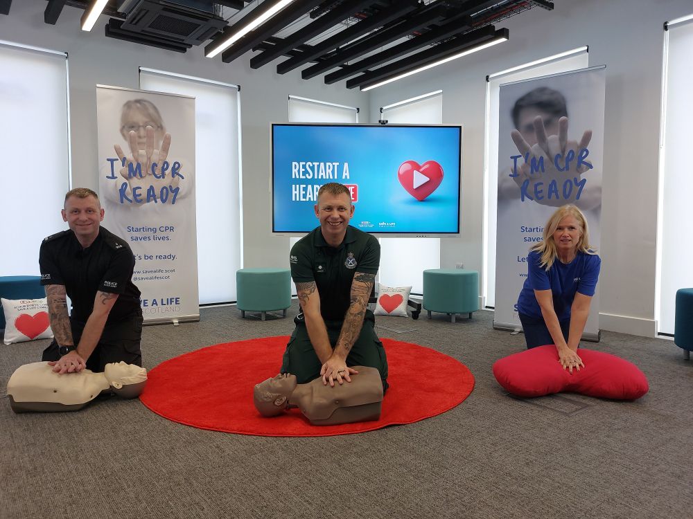 Three individuals practicing CPR on mannequins in a training room with banners promoting CPR readiness behind them.