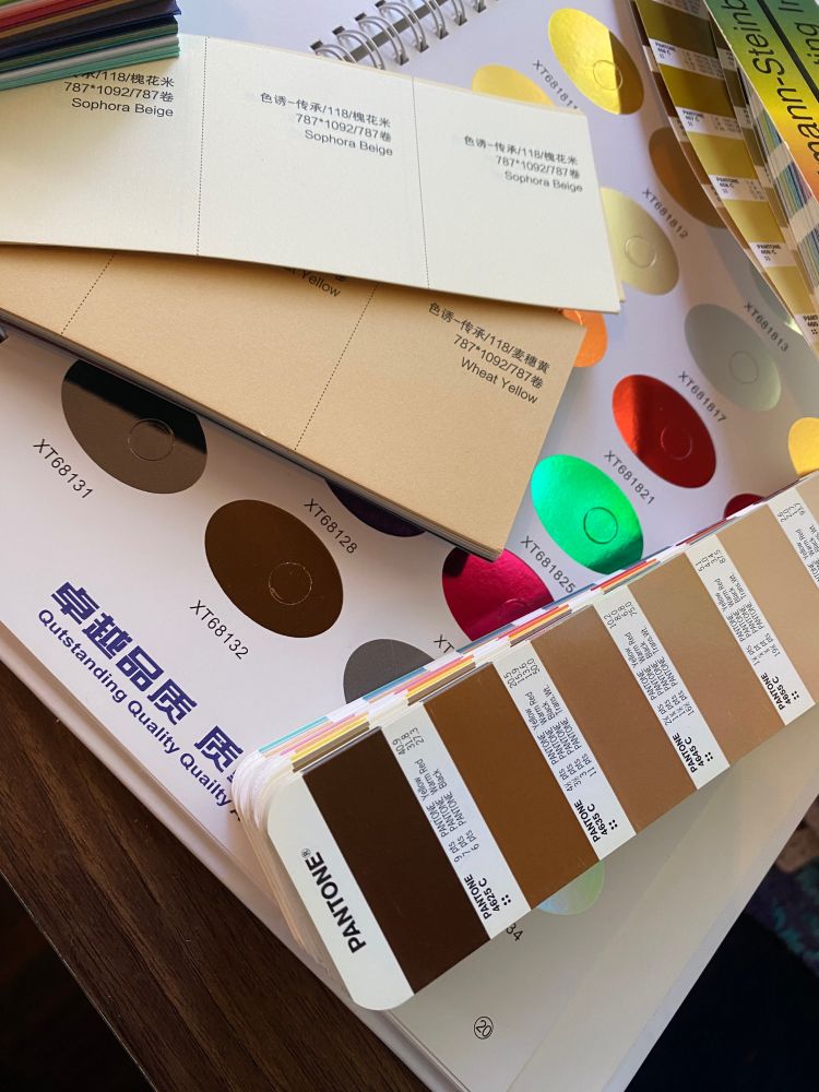 PMS ink swatches in shades of brown rest over foil samples in various rainbow colors and a pale tan case paper sample.