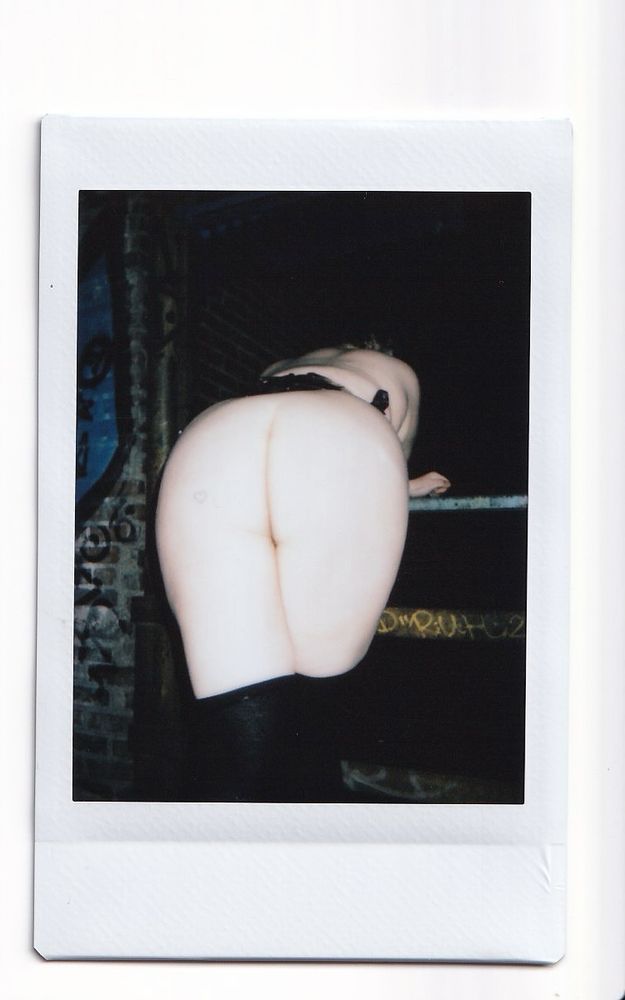 a polaroid scan of Flora’s ass, with black thigh highs and a matching corset. it is bent over in a secret alley!