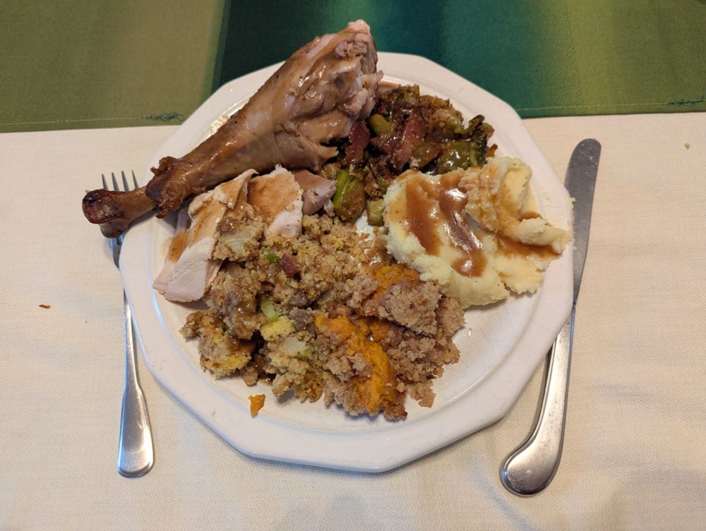 A Thanksgiving plate loaded with a turkey leg, breast meat, stuffing, sweet potatoes, mashed potatoes, and Brussels sprouts and topped with gravy.