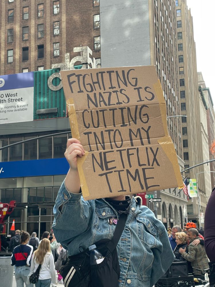Protester at the NYC #NoKings march holds a sign: “Fighting Nazis is cutting into my Netflix time.”