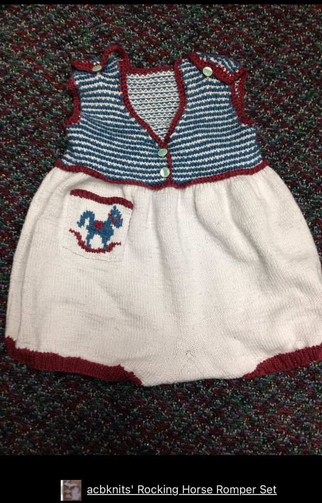 A baby’s romper in cream below the waist with blue stripes on the top and dark red trim. A rocking horse is on a pocket below the waist 