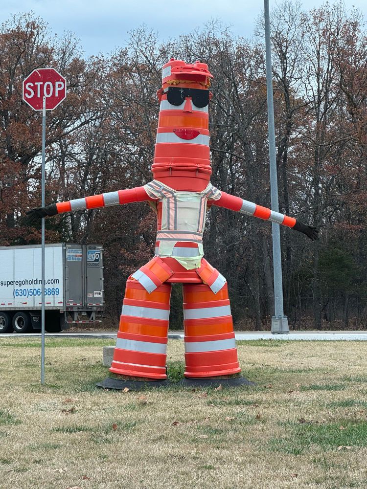 A large sculpture made of traffic cones in the shape of a man holding a tall STOP sign 