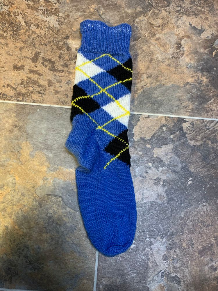 An argyle sock in blue with black and white diamonds and yellow crossings