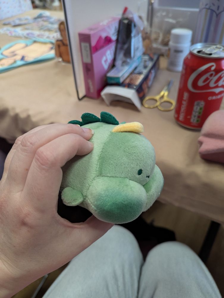 A plushy keyring of a green dinosaur that looks a bit like Godzilla with big tits