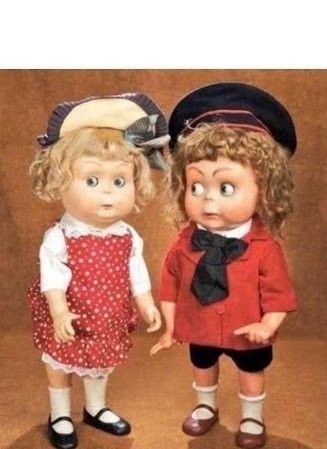 Duas bonecas antigas se entreolhando com uma cara que parece constrangimento 