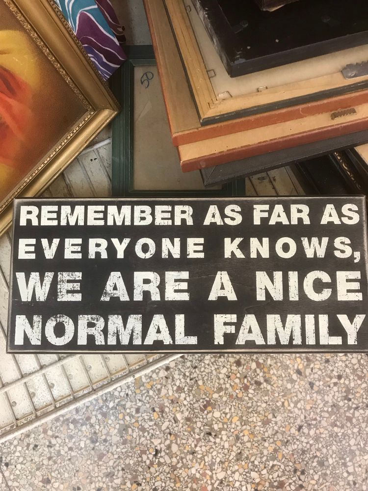 A black sign with white letters. The sign says: Remember as far as everyone knows, we are a nice normal family.