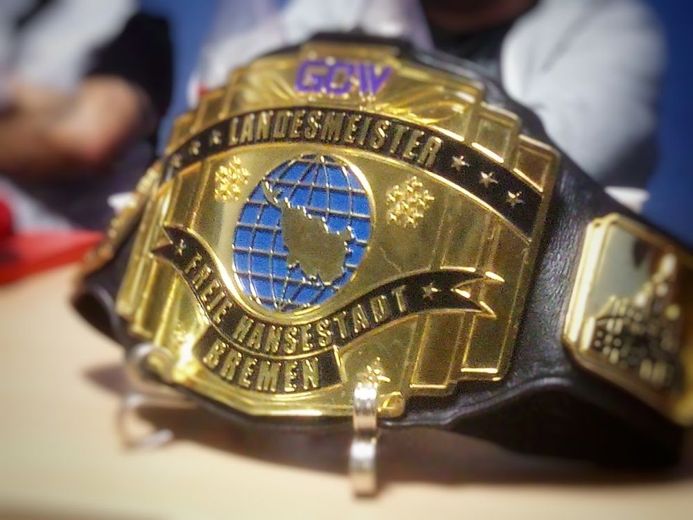 close-up photo of a golden wrestling championship belt. It shows the outlines of the city-state of Bremen with the inscription GCW LANDESMEISTER FREIE HANSESTADT BREMEN (State Champion of the Free Hanseatic City of Bremen)