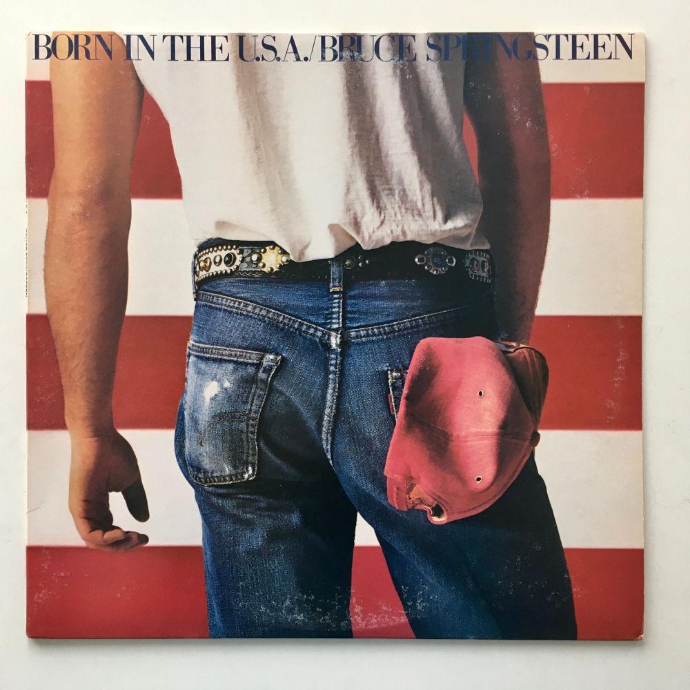 Album cover for Bruce Spingsteen's Born In The USA. The photo frames Springsteen's butt in well-worn jeans. His hips are cocked to one side. He's wearing a plain white tank top as well. There's a red baseball cap in his right back pocket, which in a gay bar would be flagging that he likes getting fisted. Mind you if he walked into a gay bar in the 70s like this he'd be instantly obliterated by everyone wanting to get their hands on him at once. He'd get men following him down the street in this outfit. It's literally saying "hey boys, come fuck me".