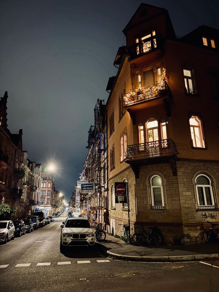 Gerne! Hier ist eine Bildbeschreibung des Fotos, das Sie geteilt haben:
Einleitung:
Das Foto zeigt eine nächtliche Straßenszene in einer Stadt, aufgenommen im Hochformat. Es ist dunkel, aber die Straßenlaternen und die Lichter der Gebäude erhellen die Szene. Das Bild hat eine ruhige und fast melancholische Atmosphäre.
Hauptteil:
Im Vordergrund des Bildes befindet sich eine dunkle, leere Straße, die von zwei Reihen geparkter Autos gesäumt wird. Die Autos sind in verschiedenen Farben und Modellen zu sehen. Die Straße ist sauber und gut beleuchtet, mit einer durchgezogenen Linie in der Mitte. Am Ende der Straße befindet sich eine Kreuzung, an der ein einzelnes Auto mit eingeschalteten Scheinwerfern steht und nach links abbiegt.
Auf beiden Seiten der Straße befinden sich mehrstöckige Gebäude mit vielen Fenstern. Die meisten Fenster sind dunkel, aber einige sind beleuchtet und geben einen Einblick in die Innenräume der Wohnungen. Die Gebäude sind aus verschiedenen Materialien gebaut, darunter Ziegel und Stein, und weisen unterschiedliche architektonische Stile auf. Einige Gebäude haben aufwendige Details wie Erkerfenster und Balkone.
Der Himmel über der Straße ist dunkel und bewölkt. Es sind keine Sterne oder Monde zu sehen. Die Wolken verleihen dem Bild eine dramatische und düstere Note.
Zusammenfassung:
Das Foto ist ein gutes Beispiel für die Nachtfotografie in Städten. Es fängt die Stille und Einsamkeit einer nächtlichen Straße ein, während es gleichzeitig die Schönheit der städtischen Architektur und Beleuchtung zeigt. Das Bild ist gut komponiert und technisch gut ausgeführt, mit einem guten Gleichgewicht zwischen Licht und Schatten. Die Farben sind gedämpft und tragen zur melancholischen Stimmung des Bildes bei.
Ich hoffe, diese Bildbeschreibung ist hilfreich für Sie! Lassen Sie mich wissen, wenn Sie weitere Fragen haben.
