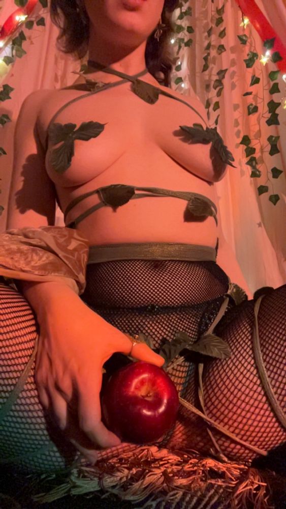 a portrayal of “Eve” sitting beneath a canopy of ivy and lights, leaves cover her breasts and fishnets cover her legs; an apple between them—as if to symbolize some “forbidden fruit”