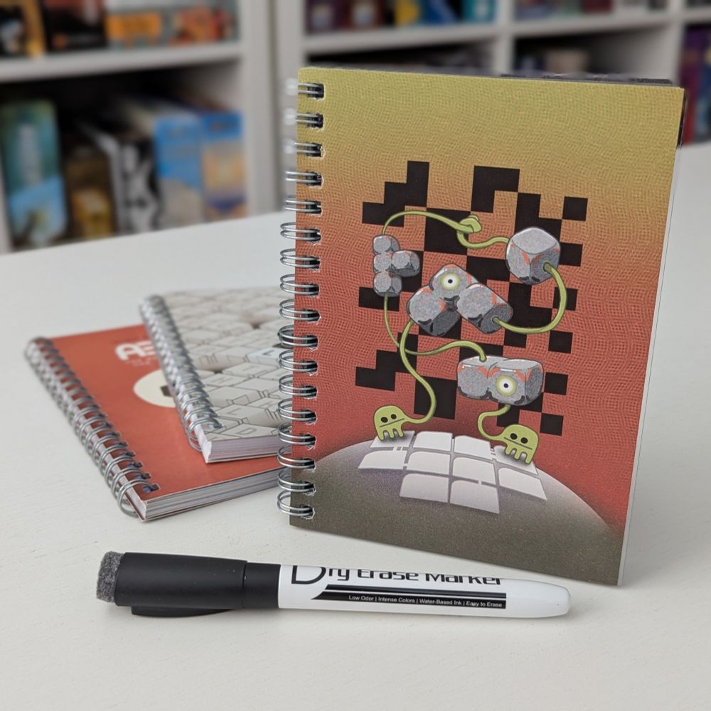 Puzzle book Workworkwork is pictured standing up next to a pile of other puzzle books - Lok and Abdec. A dry erase pen is ready to go in front of the pile of books.