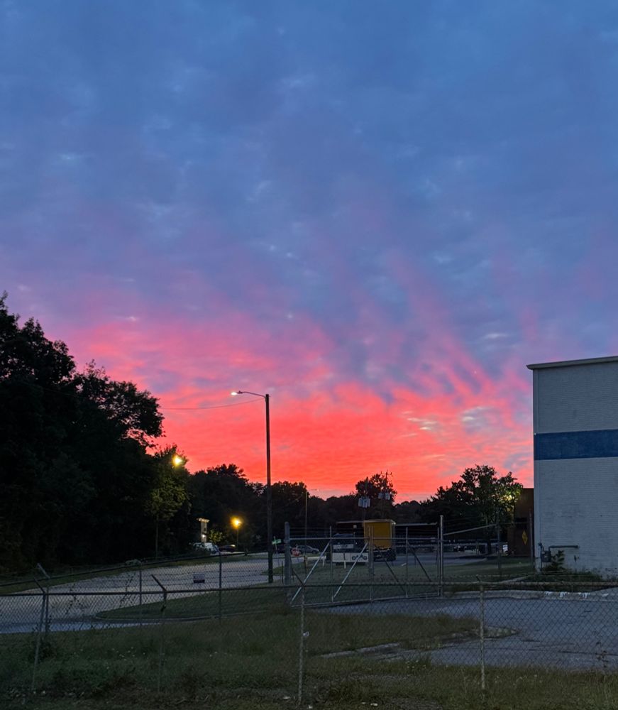 Brilliant sunrise in the distance, with a parking lot and cinderblock building in the foreground 