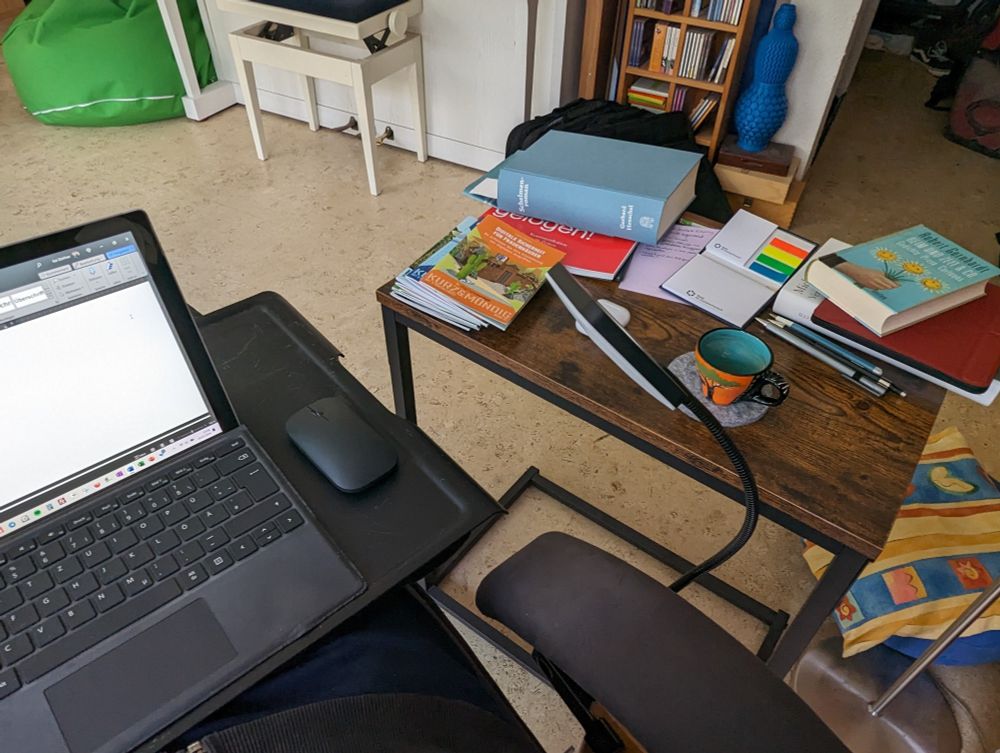 Beistelltisch mit Büchern und Tasse darauf. Laptop auf einen Kissentablett, Beine auf dem Hocker.