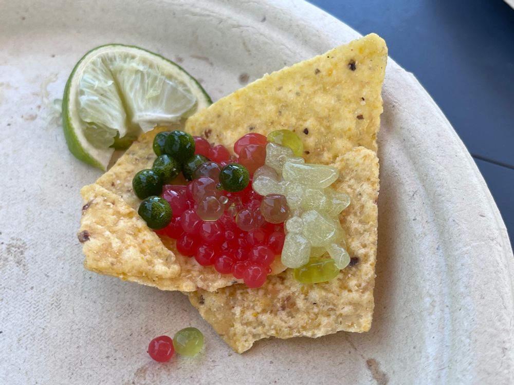 Caviar-like spheres of pink and shades of green rest on a tortilla chip. 