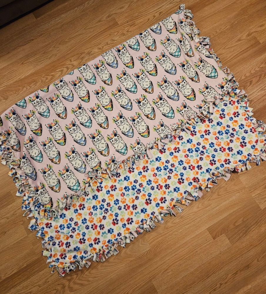 Fleece blanket tied on all sides. One side rainbow pawprints, one side colorful llamas. 