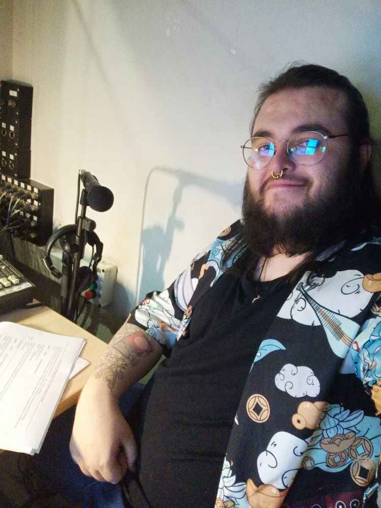 Ramón sentado nunha cabina de son cun micrófono detrás.