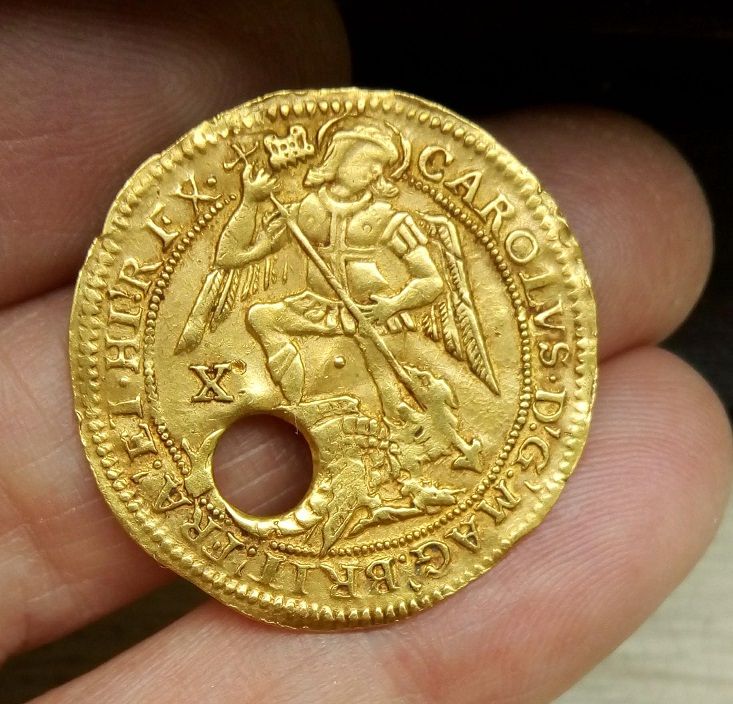 Photo of the obverse of a gold Angel coin, issued during the reign of Charles I. Angels were struck in small numbers from higher purity gold, for distribution at Royal Touching ceremonies. Those handed out at the ceremonies were officially pieced like this example, to allow them to be suspended on a ribbon. They would then be placed around the neck of a person suffering from scrofula in the hope that, as a channel for God's healing power, the King's touch would alleviate their symptoms.  