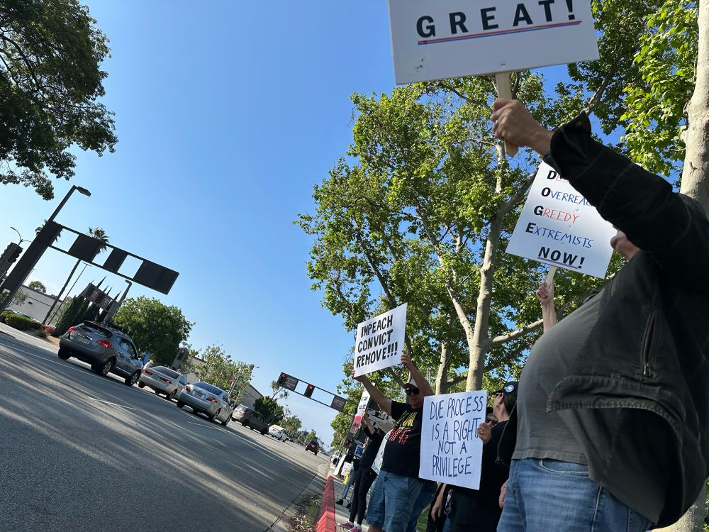 Folks standing along Clark Avenue, holding signs which read “Impeach Convict Remove!!!” and “Due Process is a Right Not a Privilege”