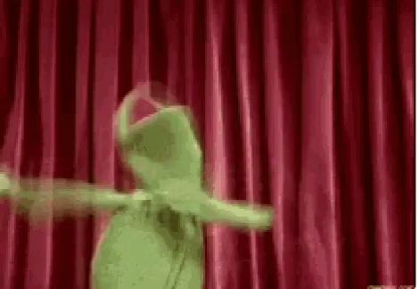 kermit the frog is dancing on a stage with a red curtain behind him .