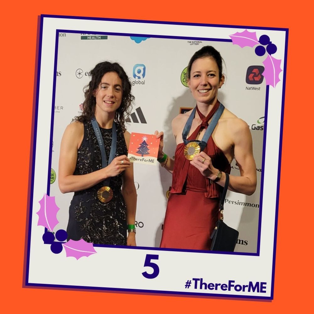 A pretend polaroid shows Emily Craig and Imogen Grant posing for a photo holding a #ThereForME Christmas card. 

The image on the card shows the dark blue Christmas tree, decorated with sparkling fairy lights, baubles and a star on the top, in a snowy landscape against a starry backdrop. The design is in the #ThereForME colours.
