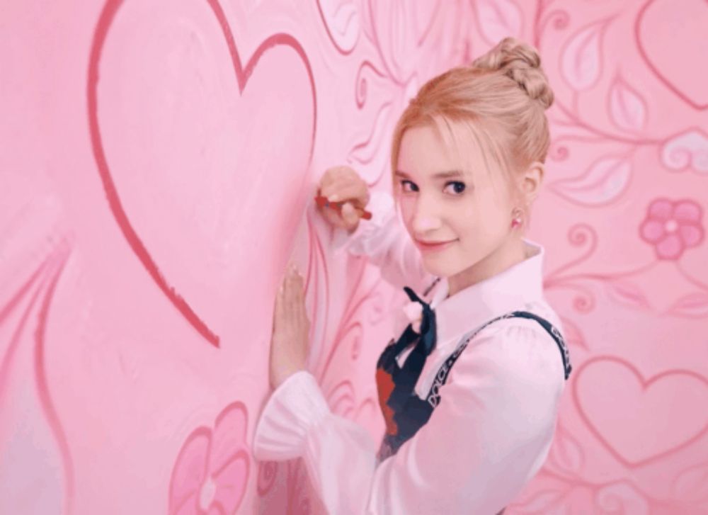 a woman draws a heart on a pink wall with a red marker