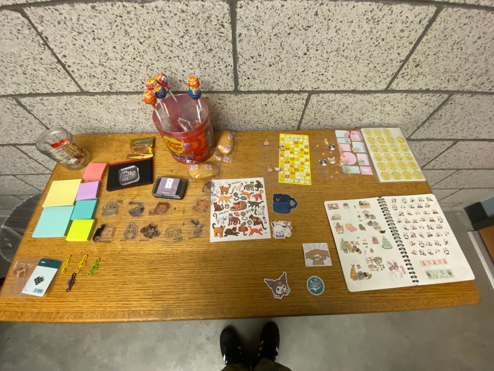 A wooden table with many things on it. There are stamps, stickers, and lollipops to name a few. 