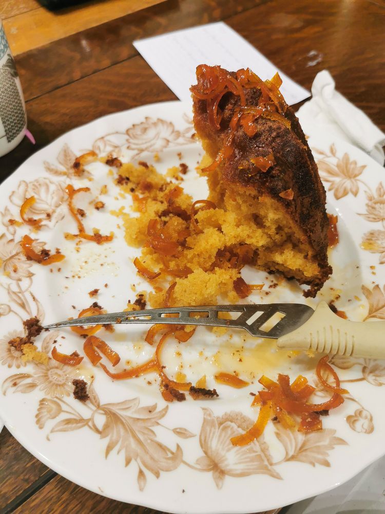 A porcelain floral plate with a knife and the remains of a marmalade bundt cake topped with candied orange peel. 