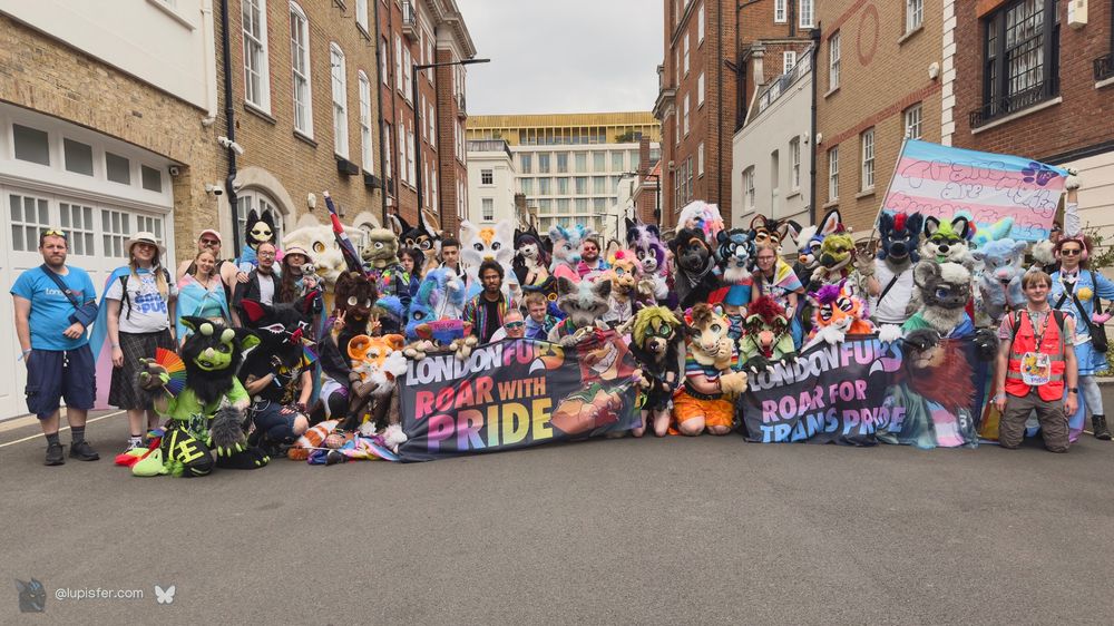 A group of 60-odd furries holding banners and flags representing LondonFurs and our diverse community, just before heading into the parade.