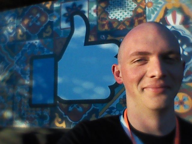 2015 pic of Tay about a month after I first shaved my head, in front of the Facebook thumbs up sign at their headquarters in the bay area