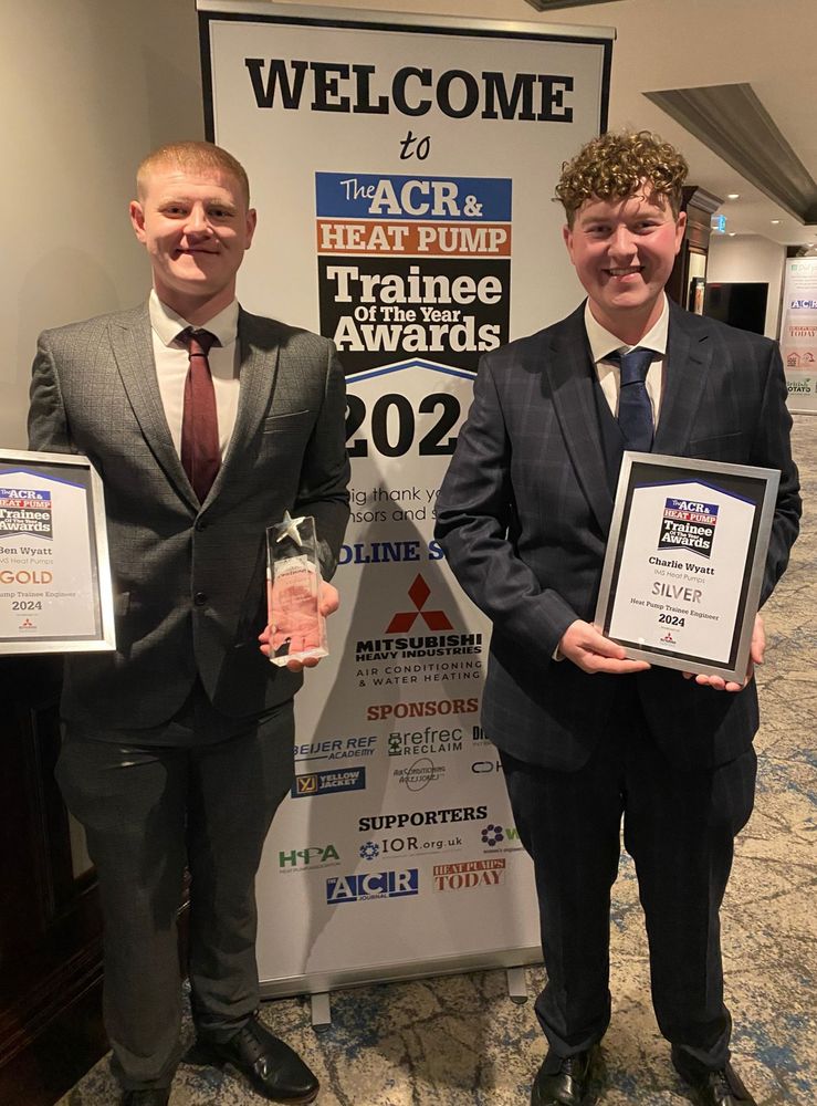 Two suited men stand together, showcasing their awards against a backdrop of a banner.