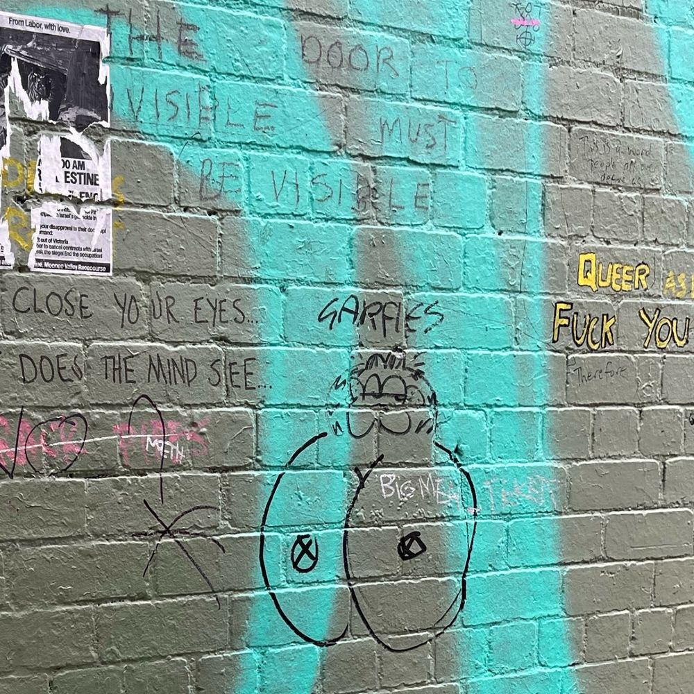 a painted brick wall tagged with a sharpie drawing of Garfield’s head on a pair of two incredibly large titties with x-es for nipples