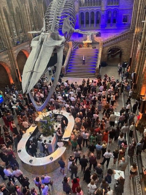 Image depicts a crowd of people celebrating inside the Natural History Museum