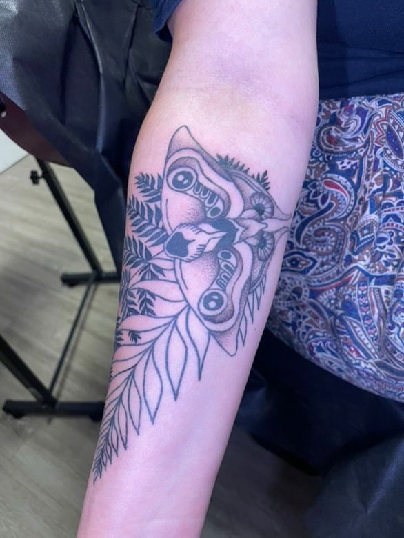 a tattoo of a moth in black ink, with minimal shading and white plant leaves