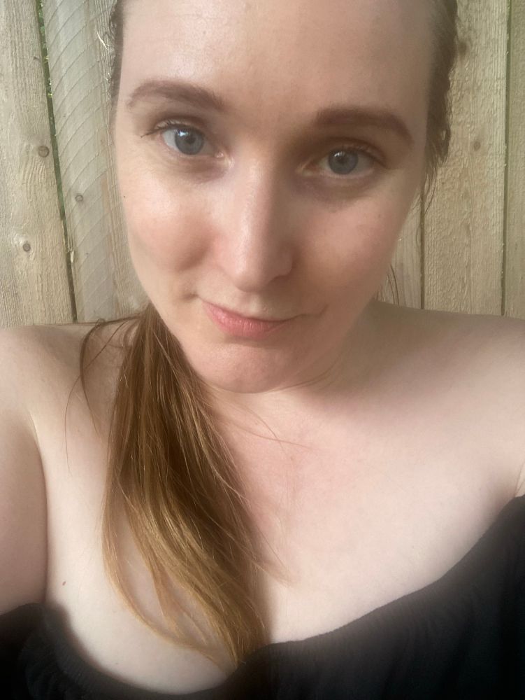 A blonde haired blue eyed pale woman in an off the shoulder black dress and her hair pulled back in a ponytail 