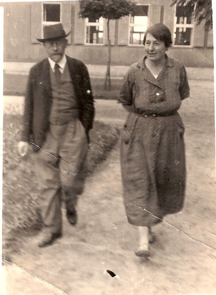 Aufnahme zweier auf den Betrachter zugehenden Menschen. Links Janusz Korczak in Anzug und Krawatte mit Hut. Rechts, mit etwas Abstand, Stefania Wilczyńska mit hinter dem Körper verschränkten Armen.