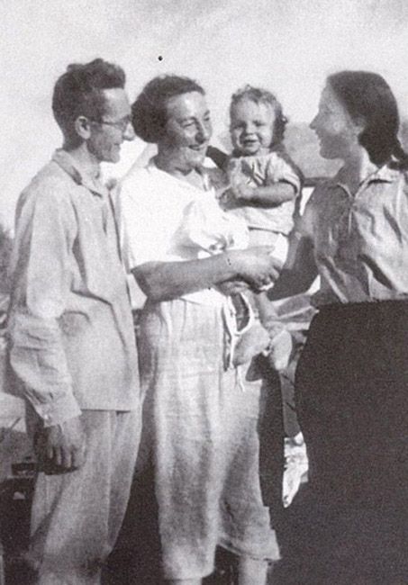 Gruppenfoto - Aufnahme wahrscheinlich im Kibbutz Ein Harod zwischen 1935 und 1939. Stefania Wilczyńska steht lächelnd mit einem etwa einjährigen Kind auf dem linken Arm im Zentrum des Bildes und blickt zu einer links neben ihr stehenden jungen Frau. Das Kind schaut direkt in die Kamera. Rechts neben Stefania Wilczyńska steht ein Mann und schaut zu dem Kind.